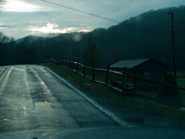 A road past a fence and a small house